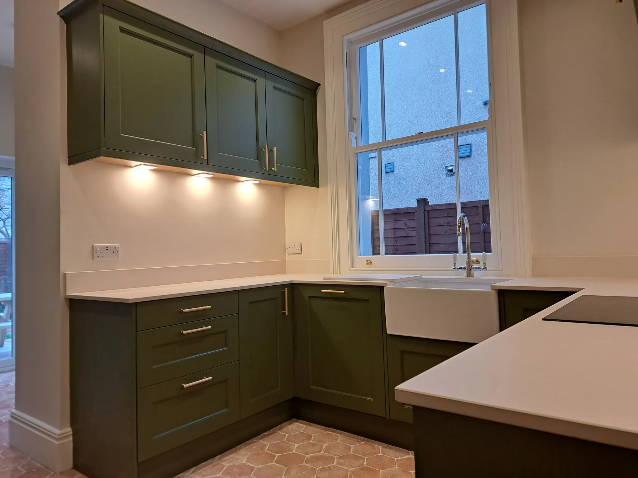 A kitchen with green cabinets and white counter tops.
