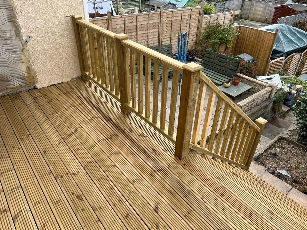 A wooden deck in a backyard next to a fence.